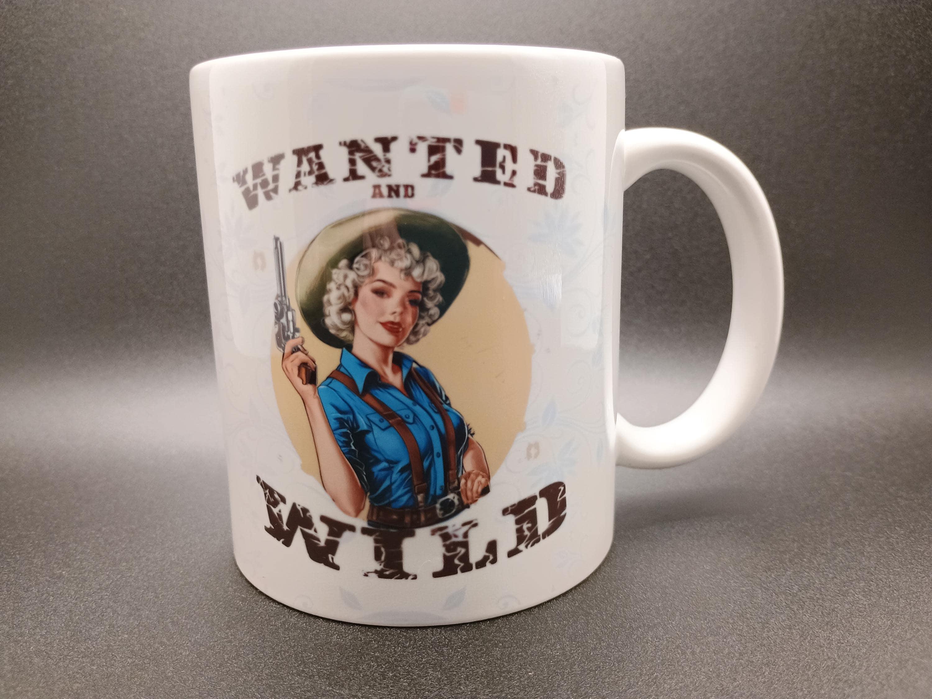 White mug with vintage pin-up cowgirl holding a revolver and text Wanted and Wild