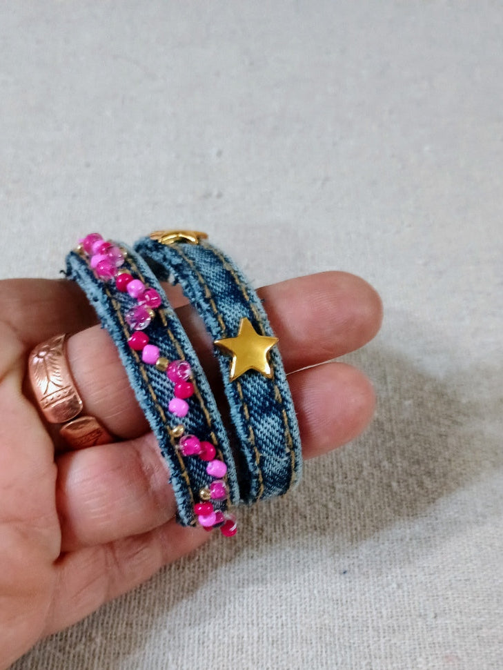 Hand holding a denim bracelet with pink beads and a gold star charm on a neutral background