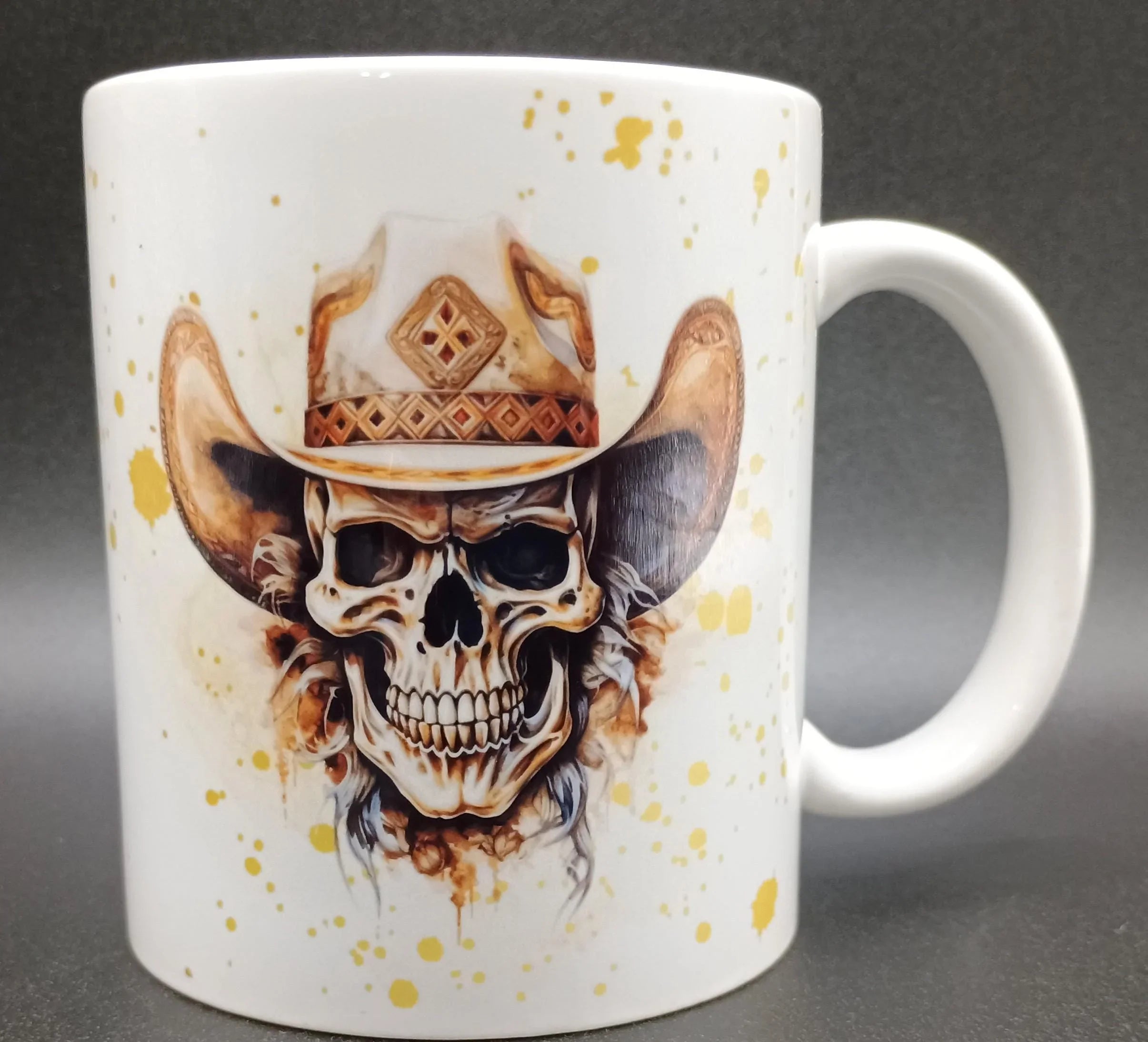 White ceramic mug featuring a detailed skull wearing a decorated cowboy hat with yellow splatter accents