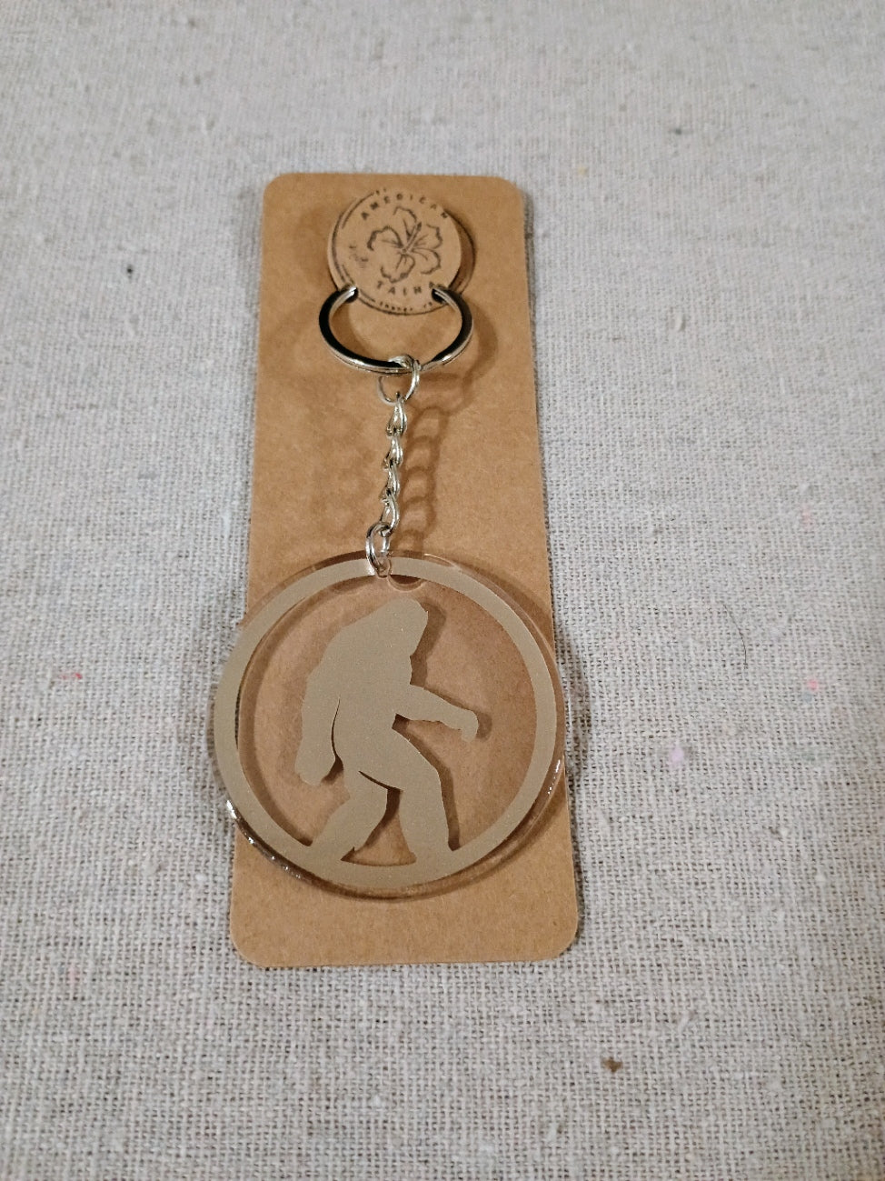 Metallic sasquatch keychain on a cardboard backing with a floral design.