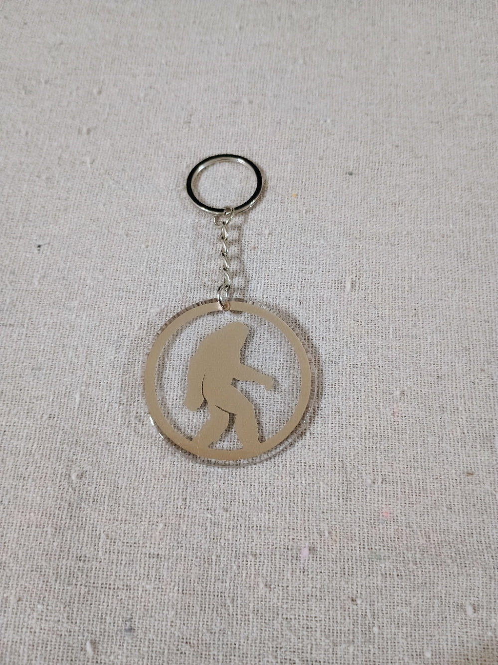 Keychain with a silhouette of a bigfoot in a circle on a textured gray background