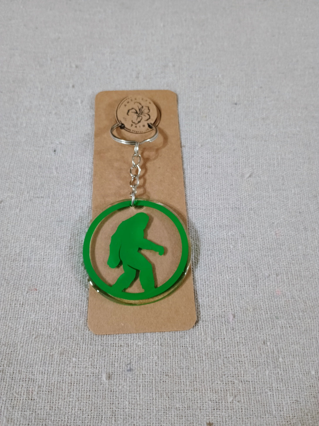 Green keychain with a silhouette of a bigfoot on a beige card against a gray background