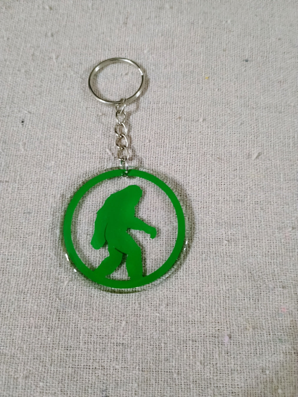 Keychain with green silhouette of a bigfoot in a circle on a gray background
