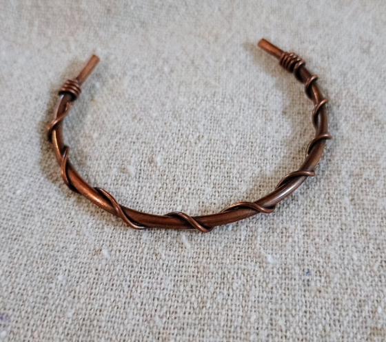 Twisted bare copper wire open cuff bracelet on linen surface