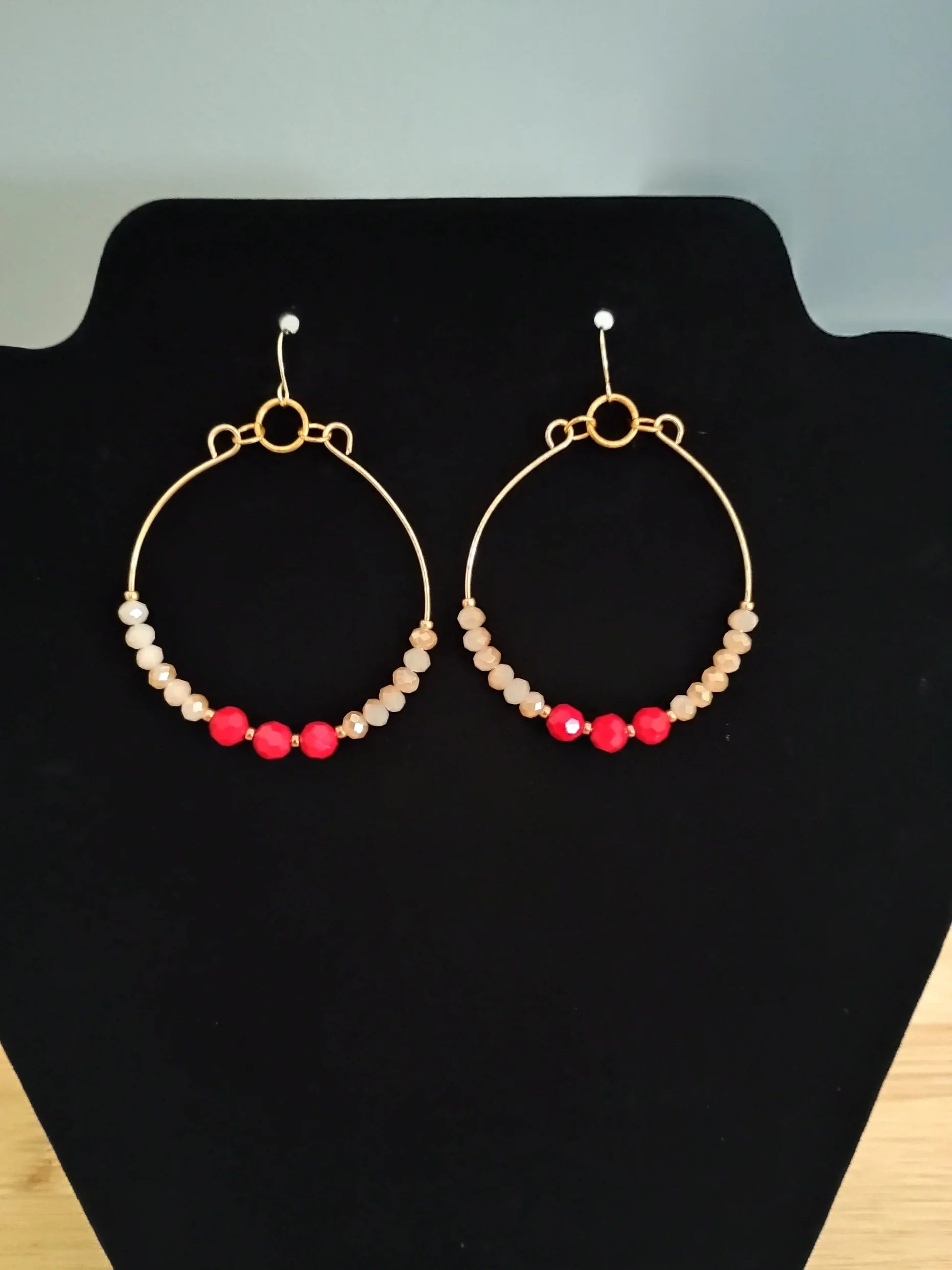 Gold hoop earrings with beige and red faceted beads displayed on black stand