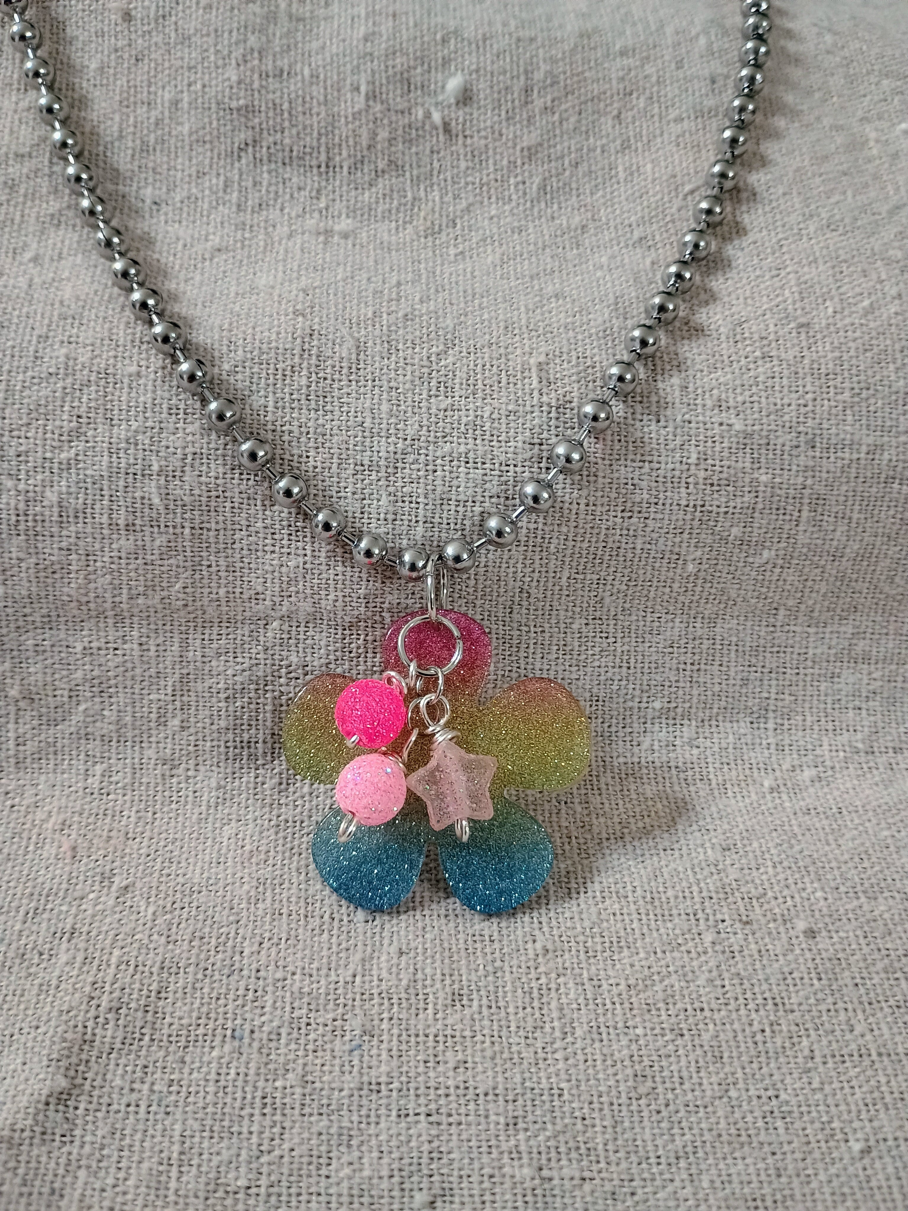 Handcrafted beaded necklace with a multicolor glitter flower pendant and pink beads on a textured fabric background