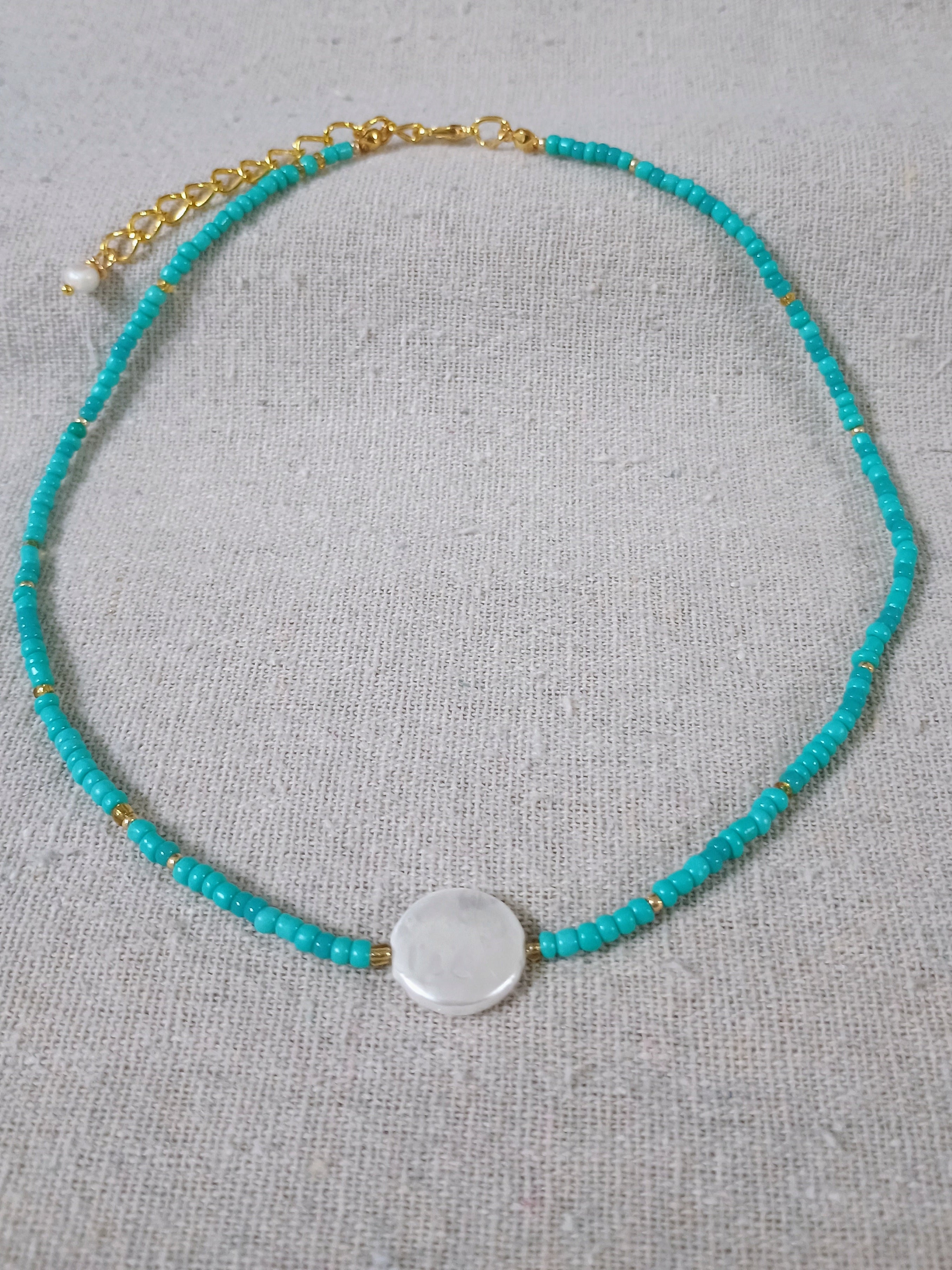 Turquoise beaded necklace with a circular pendant on a light gray background