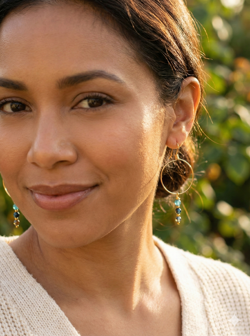 Close-up of woman wearing gold hoop earrings with blue beads in natural outdoor sunlight