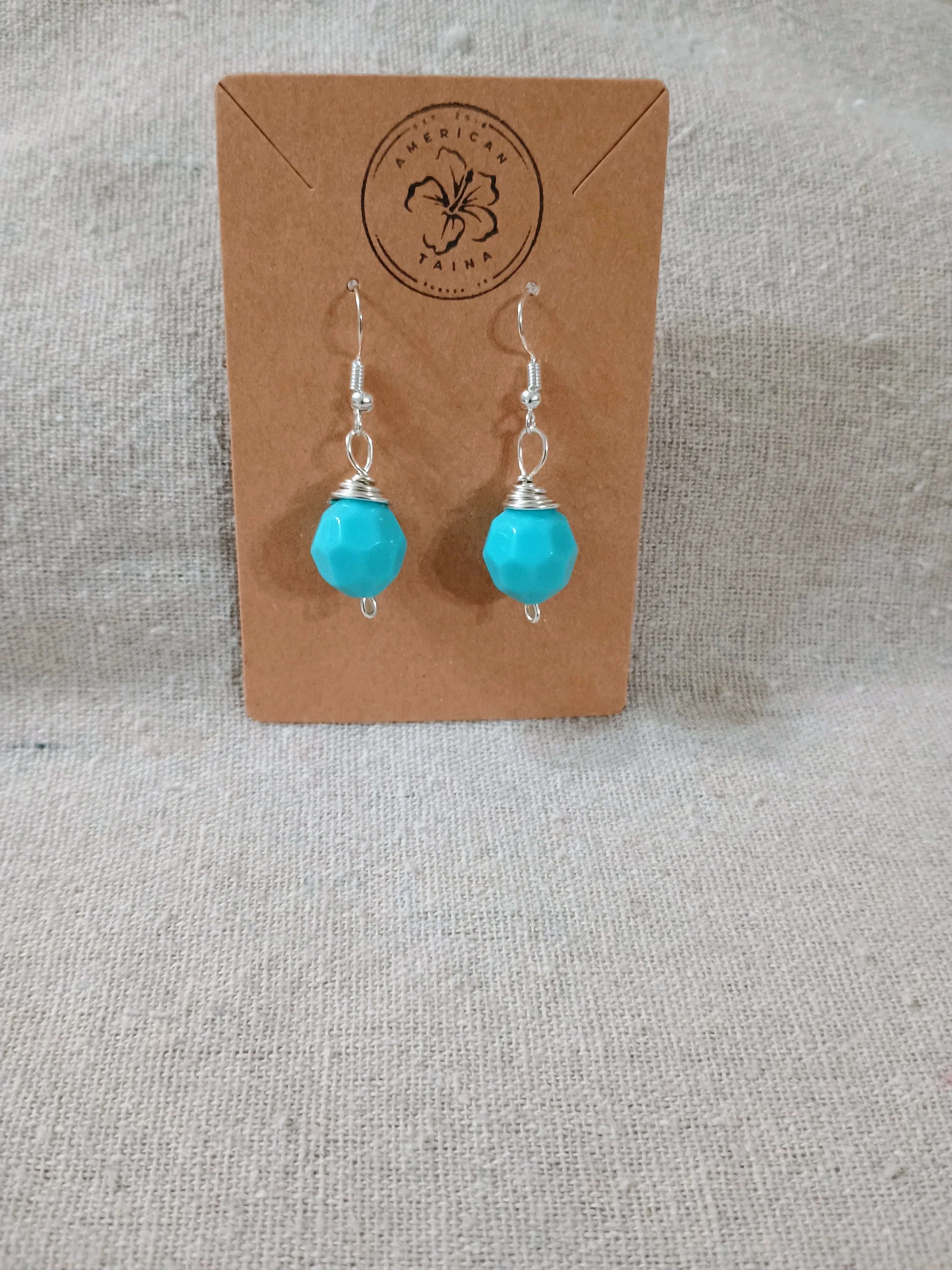Handcrafted turquoise bead earrings with silver wire hooks displayed on a brown kraft card from American Taina Crafts