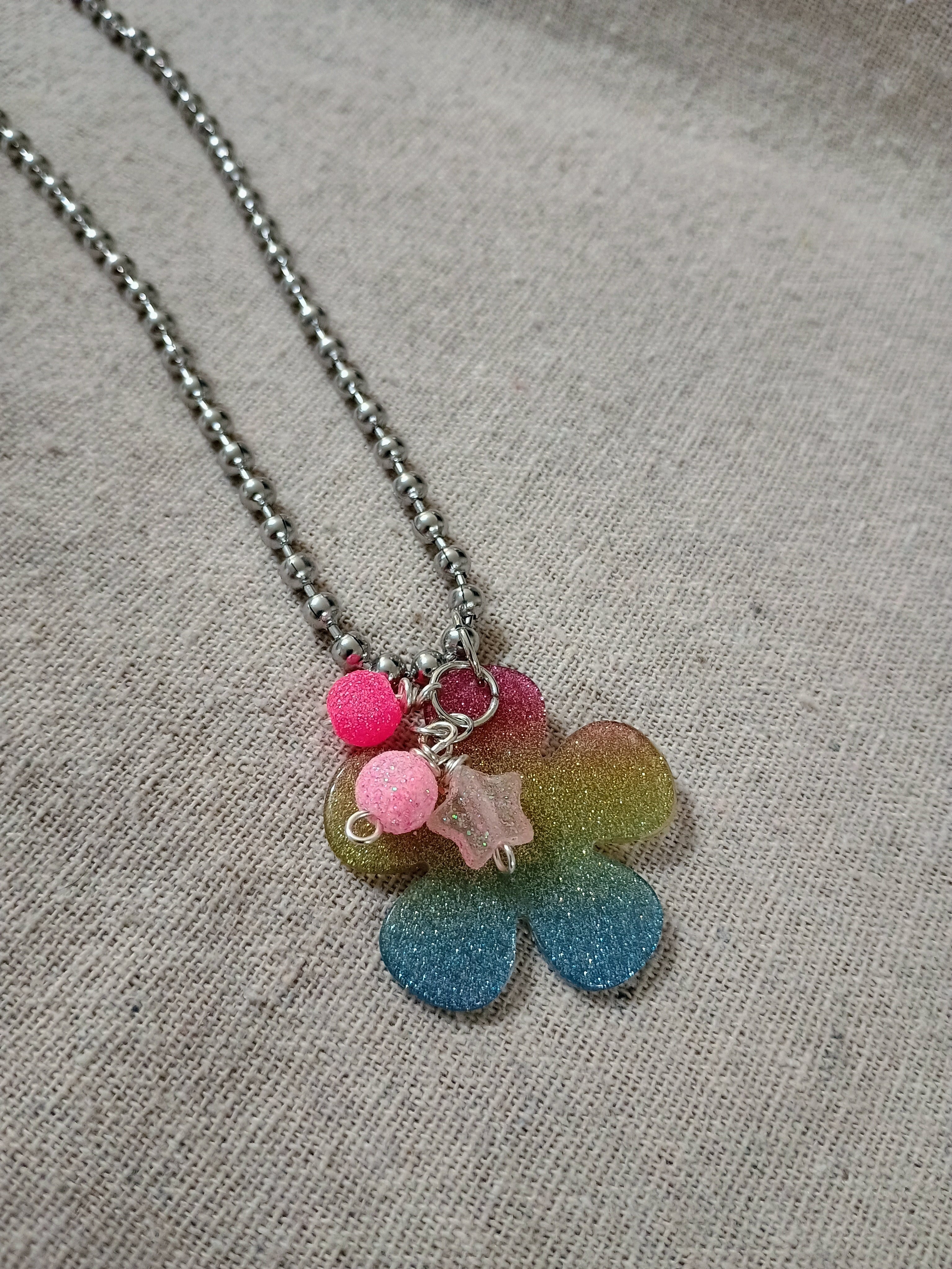 Handcrafted rainbow glitter flower pendant necklace with pink beads on silver ball chain on fabric