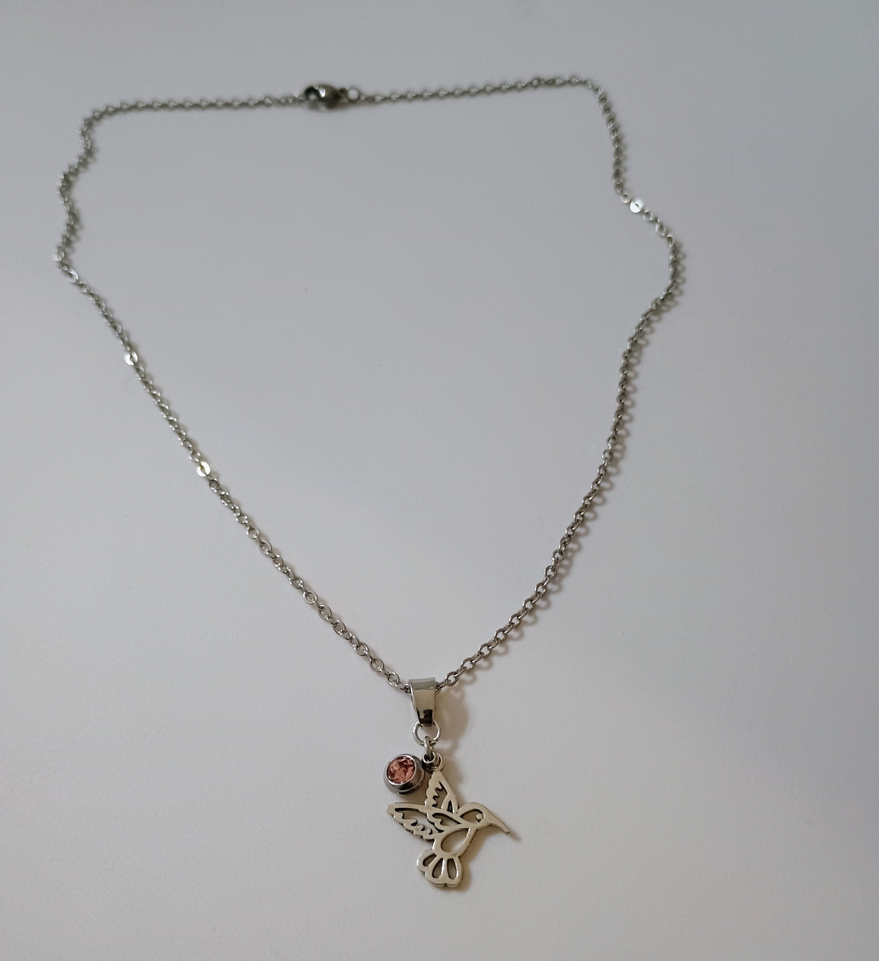 Silver chain necklace with hummingbird pendant and small pink gemstone charm on white background