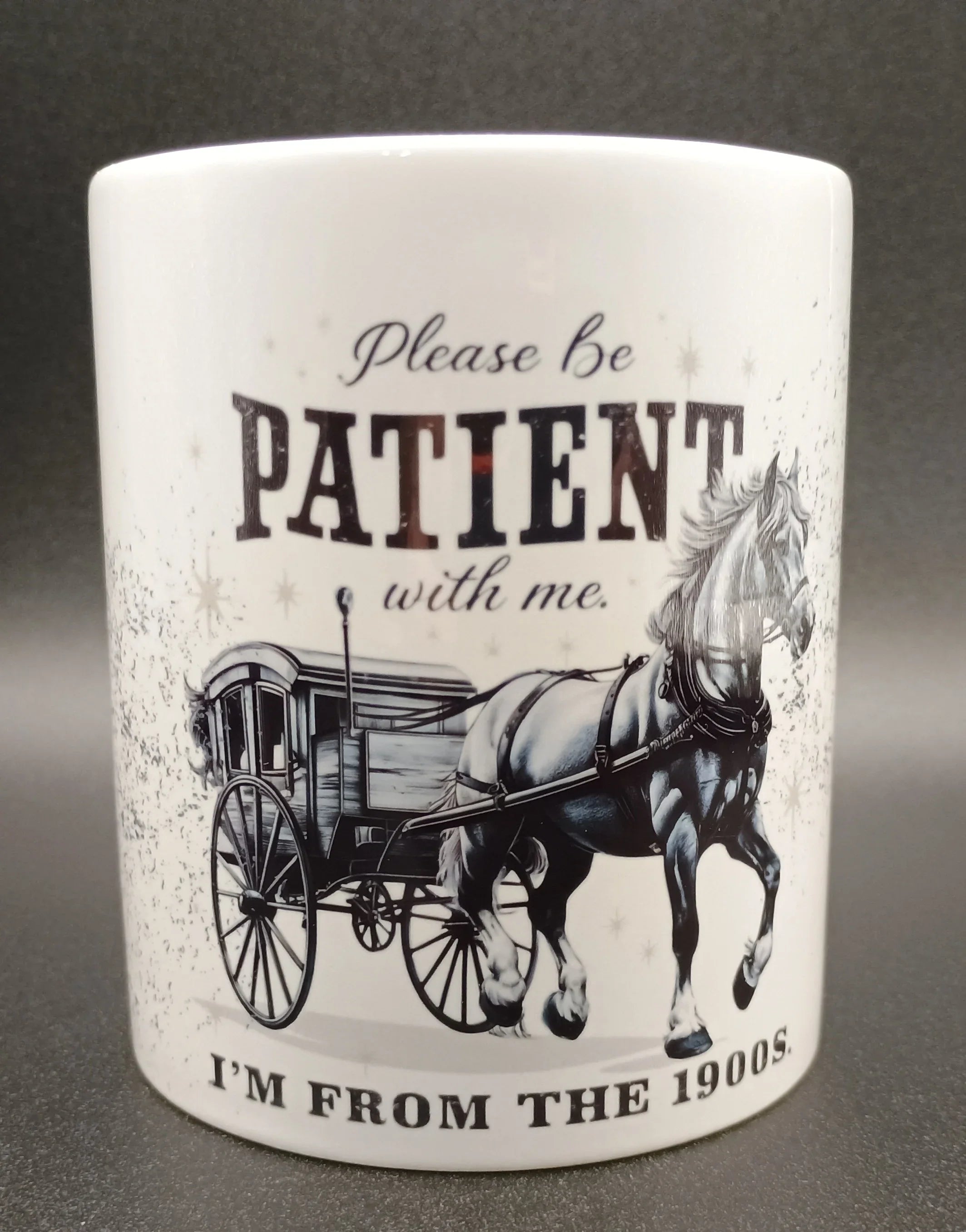 White mug with vintage horse-drawn carriage and text asking to be patient, from the 1900s