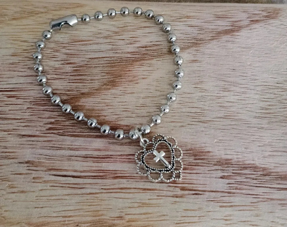 Silver beaded bracelet with heart-shaped charm featuring a cross, on wooden surface