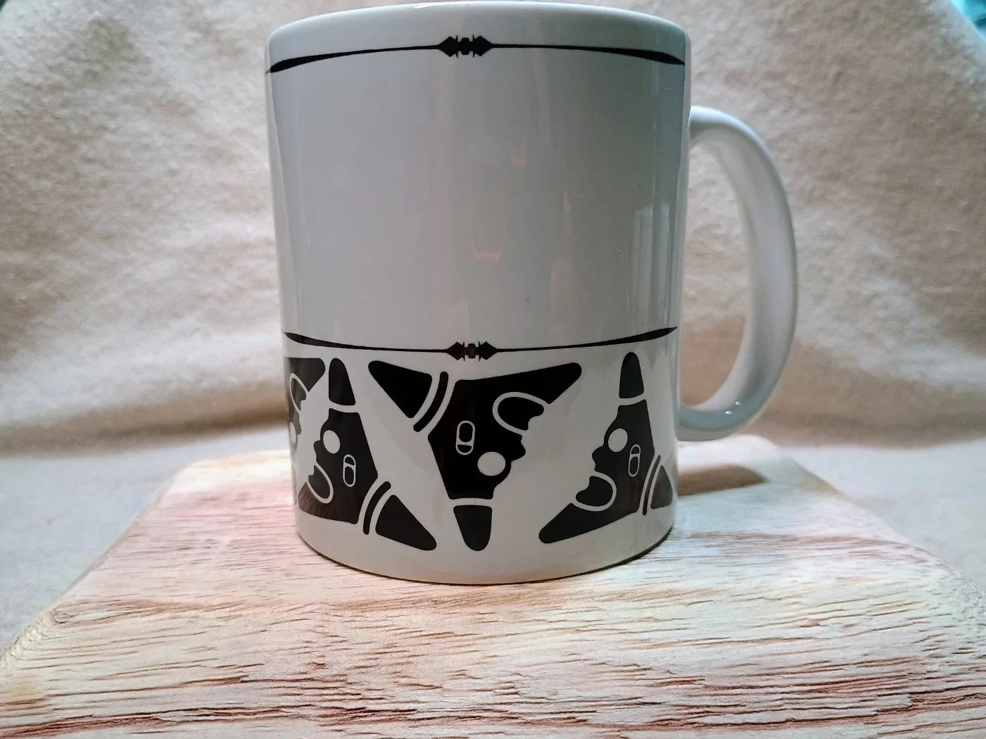 White ceramic mug with black Taíno tribal face designs on wooden surface