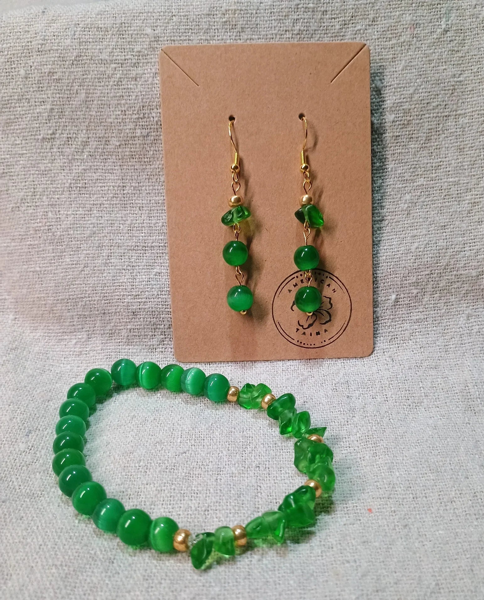 Green beaded bracelet and matching dangle earrings on beige fabric backdrop